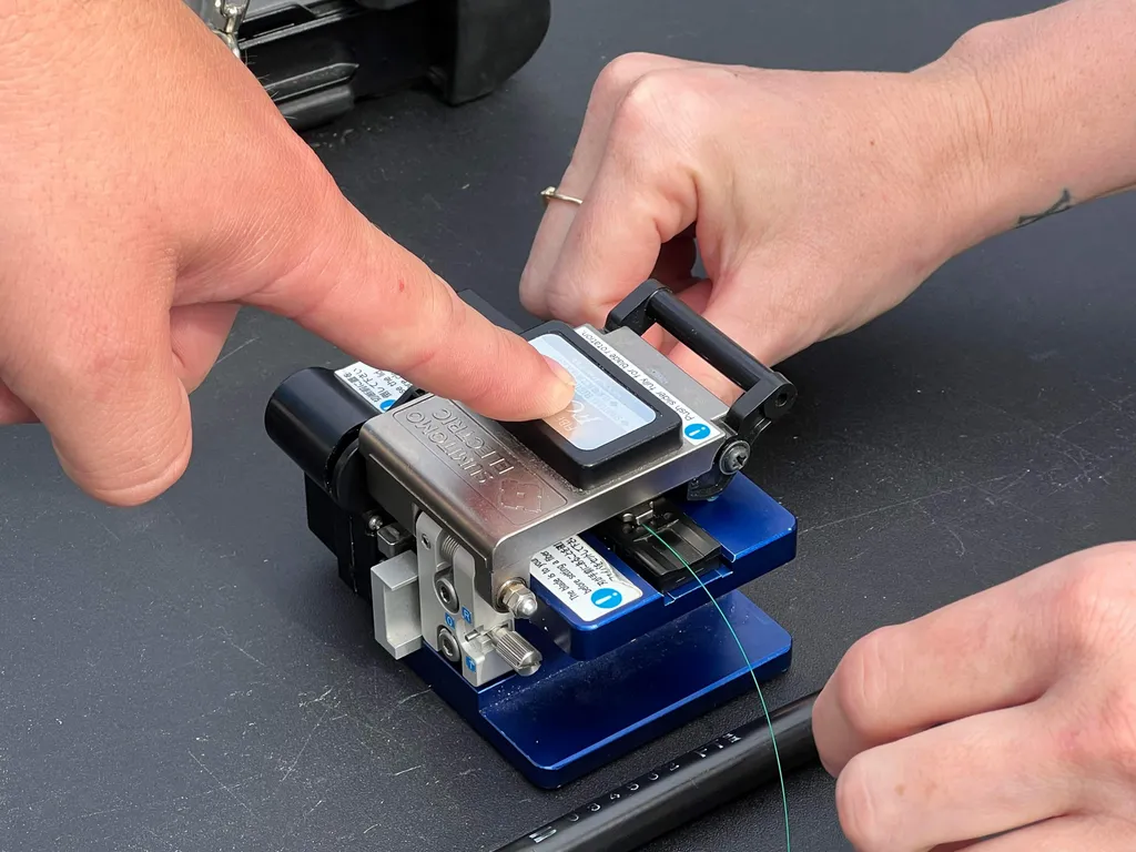 Close-up of hands using a fibre-optic splicer to join a strand of fibre cable during a rural broadband installation demonstration by Easton Utilities at a USDA Rural Development telecommunications event.