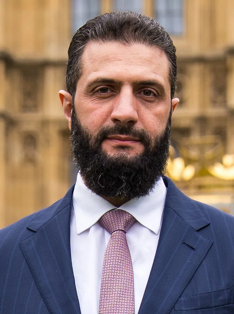 Syrian President Ahmed al-Sharaa, bearded in a dark suit and patterned tie, photographed during his UK visit in March 2026.