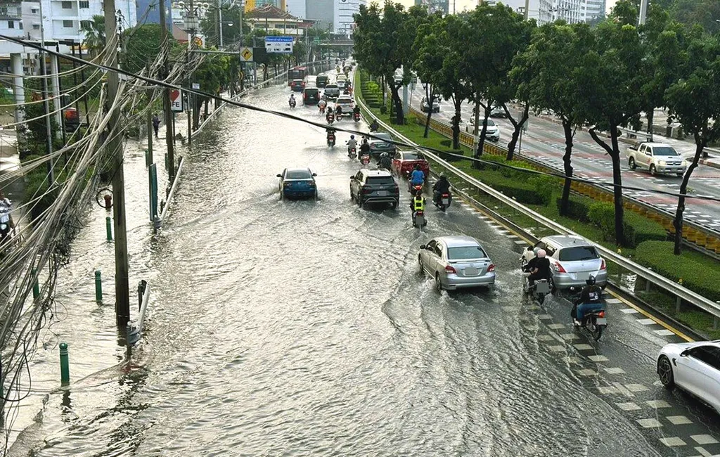 Motorbikes and cars wading through flood water on a Bangkok street during heavy flooding.