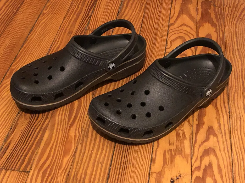 A pair of black Crocs-style clogs with perforated fronts on a wooden floor