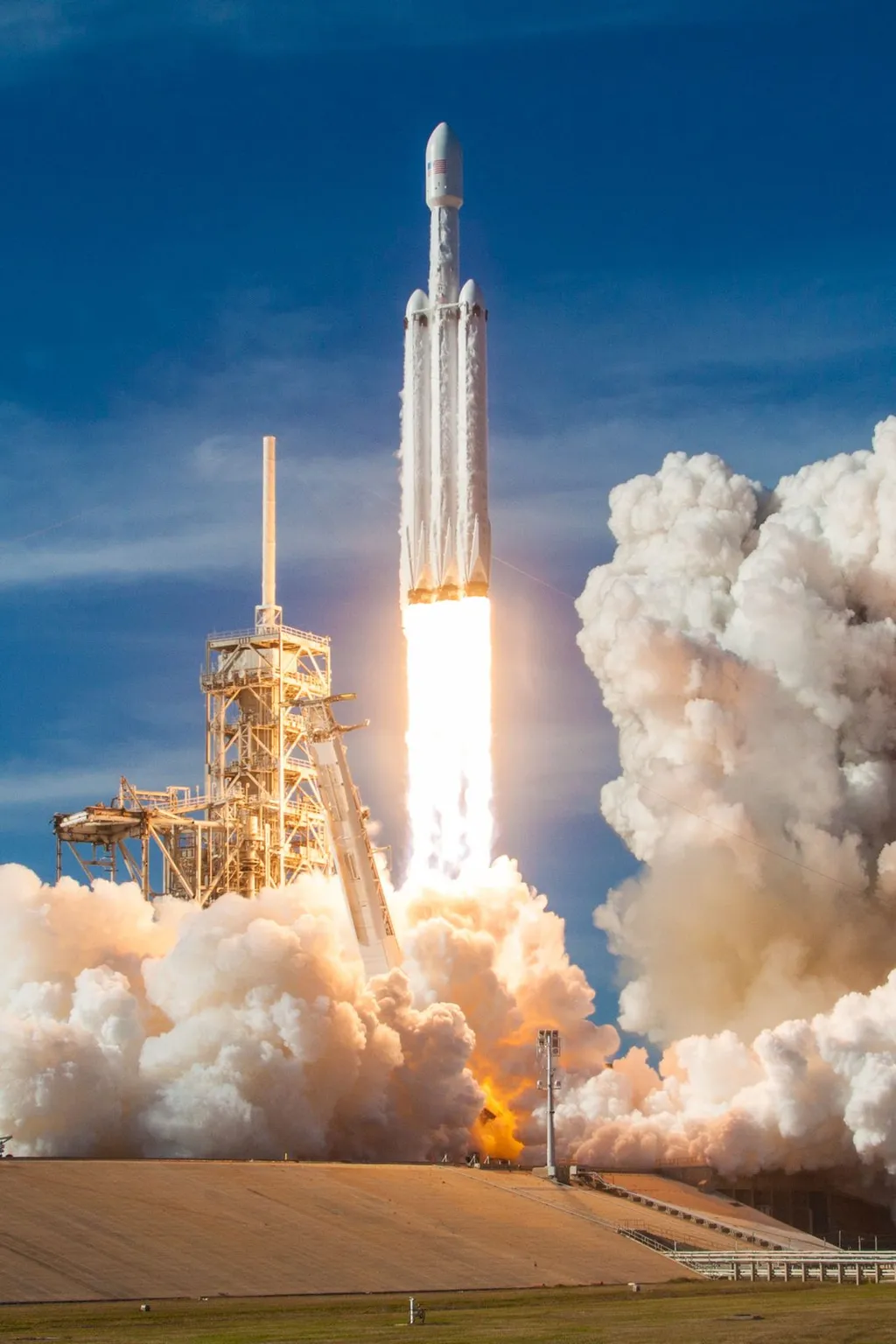 A SpaceX Falcon Heavy triple-core rocket lifting off from launch pad 39A, its three boosters trailing bright exhaust plumes and clouds of smoke.
