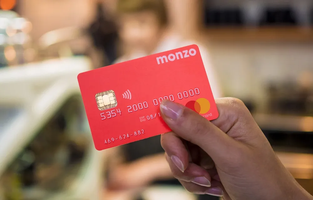 A Monzo coral debit card showing the Monzo wordmark, chip and Mastercard logo