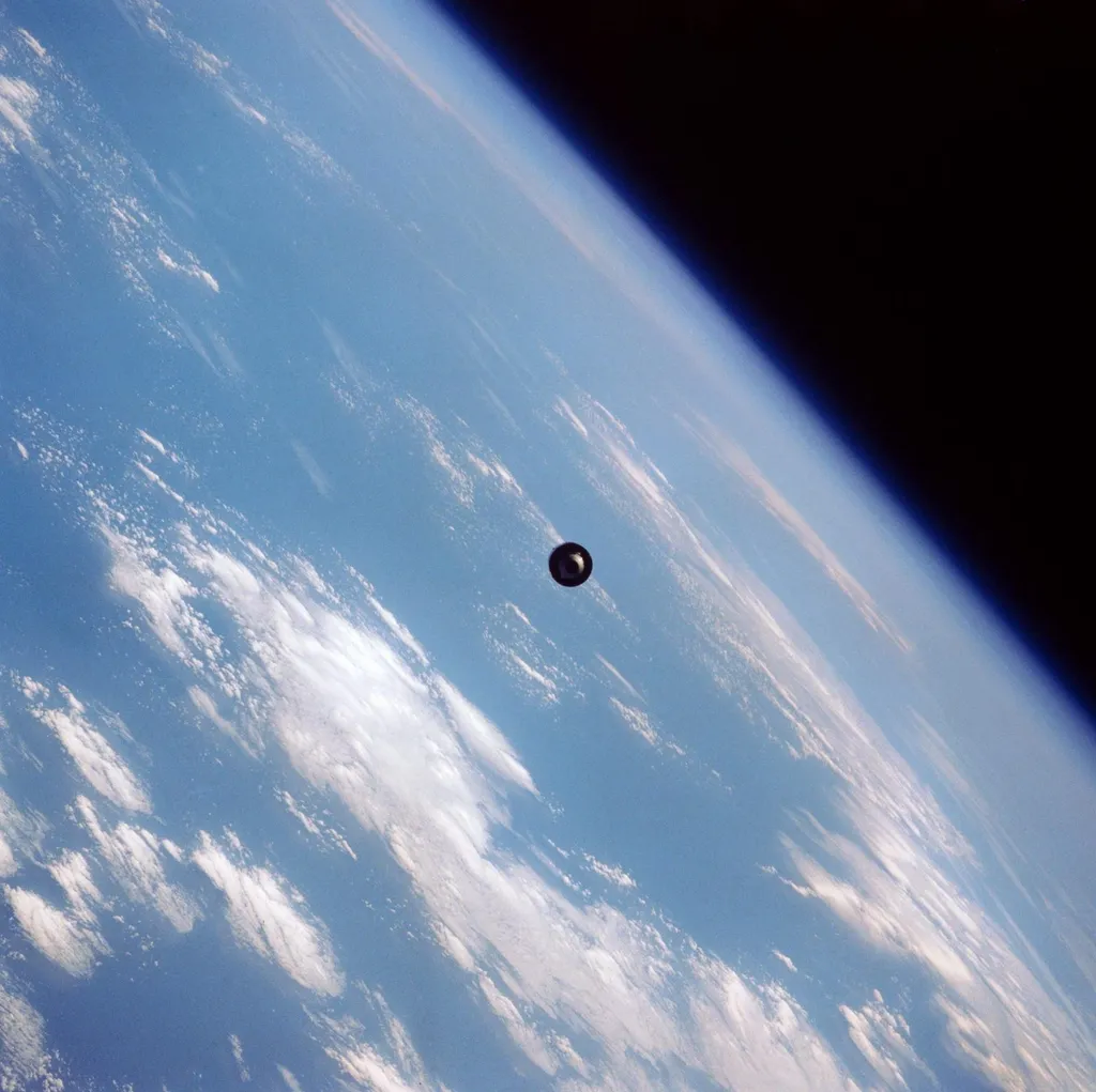 A communications satellite drifting above Earth's atmosphere, photographed from the Space Shuttle Discovery after deployment, with Earth's curved horizon below.