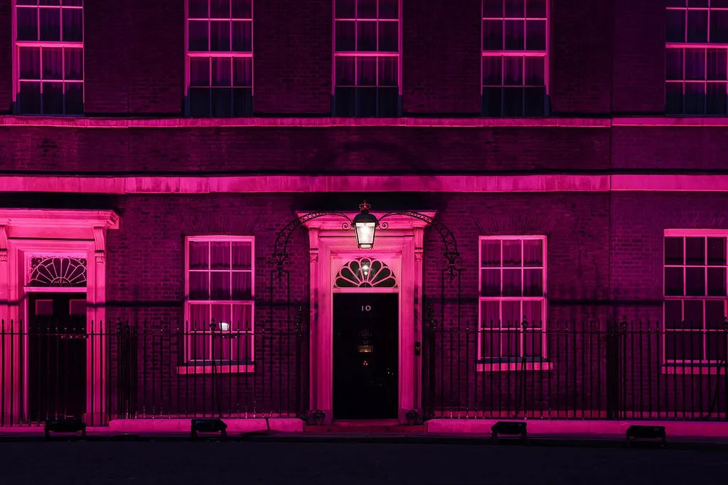 The front door of 10 Downing Street in London, its brickwork lit pink at night, with the number 10 visible on the door