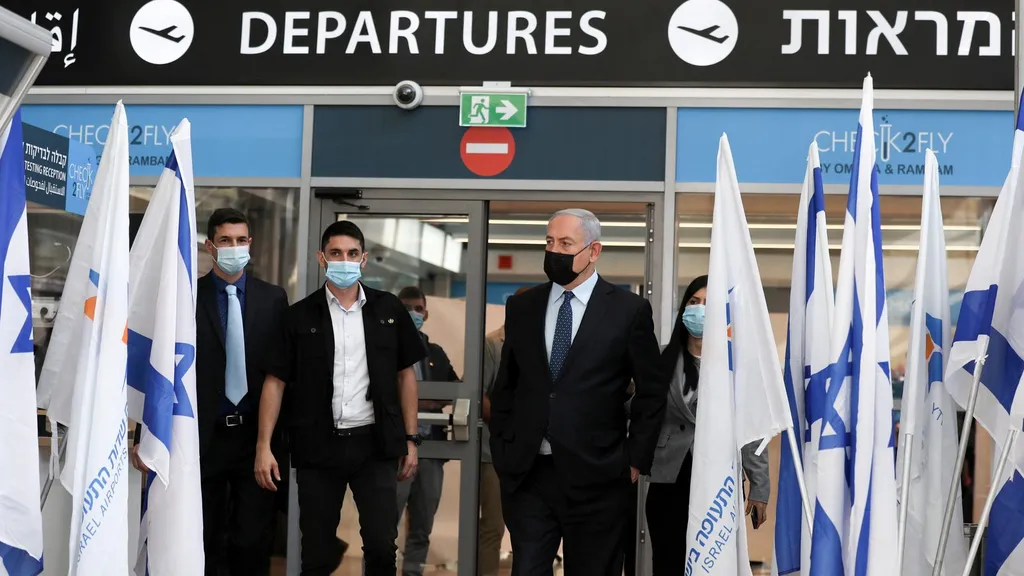 Benjamin Netanyahu walking through an airport departures hall lined with Israeli flags