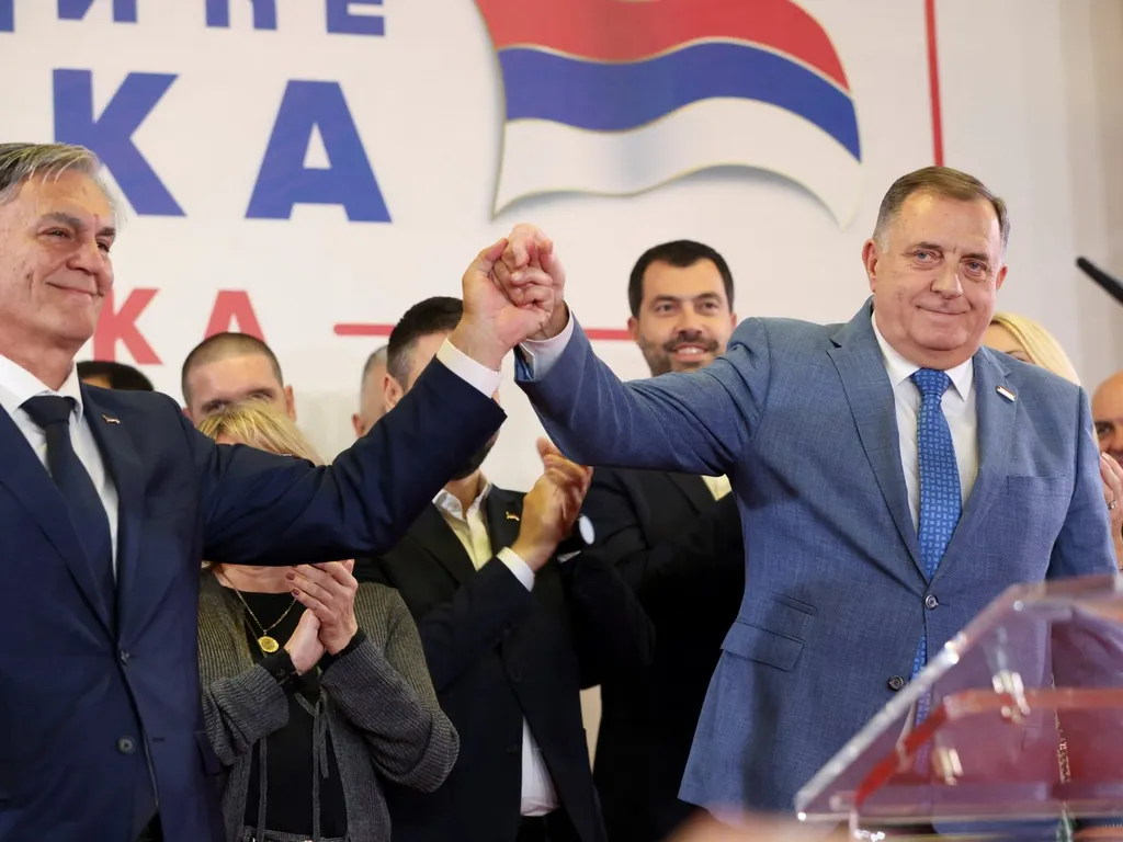 Milorad Dodik raises a joined hand with an ally at an election victory rally