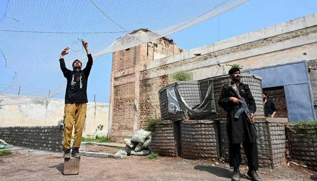 A Pakistani policeman strings a fishing net overhead at a security outpost while an armed colleague stands guard