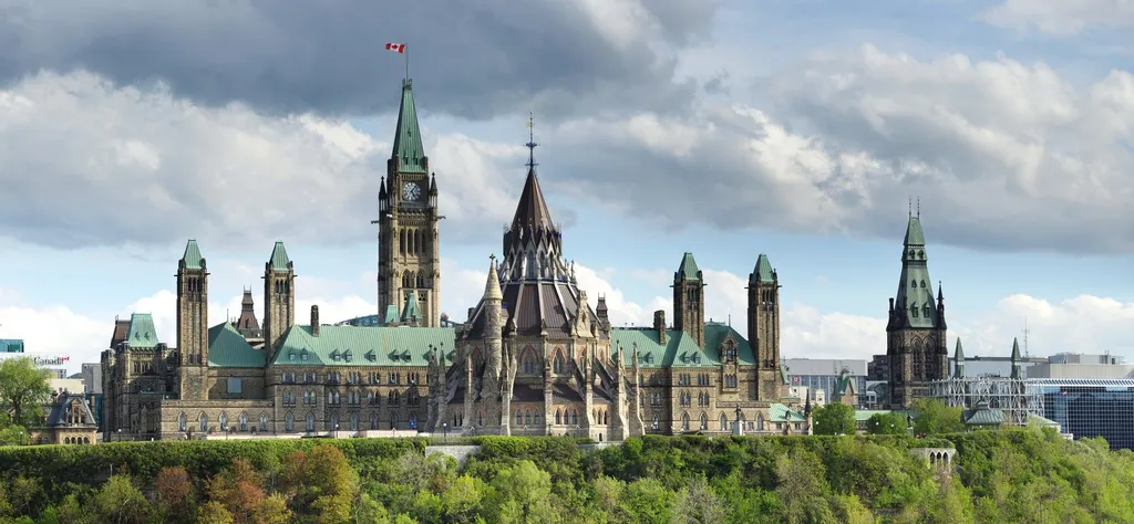 Parliament Hill in Ottawa, seen from across the river: Centre Block with the Peace Tower flying the Canadian flag, and the Library of Parliament's domed reading room in the foreground