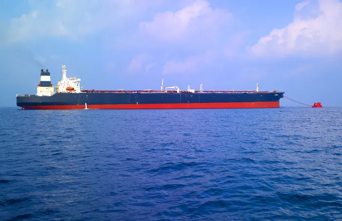 A very large crude carrier tanker with a red and black hull moored at sea beside a red single buoy mooring marker under a clear sky.