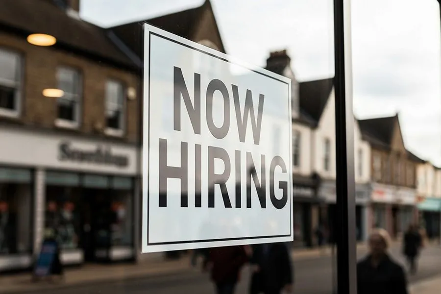 A 'Now Hiring' sign displayed in a UK high-street shop window