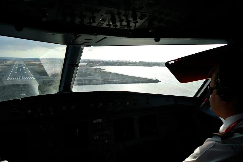 Cockpit view of an aircraft on final approach to Aden International Airport in Yemen, with the runway visible beside the sea.