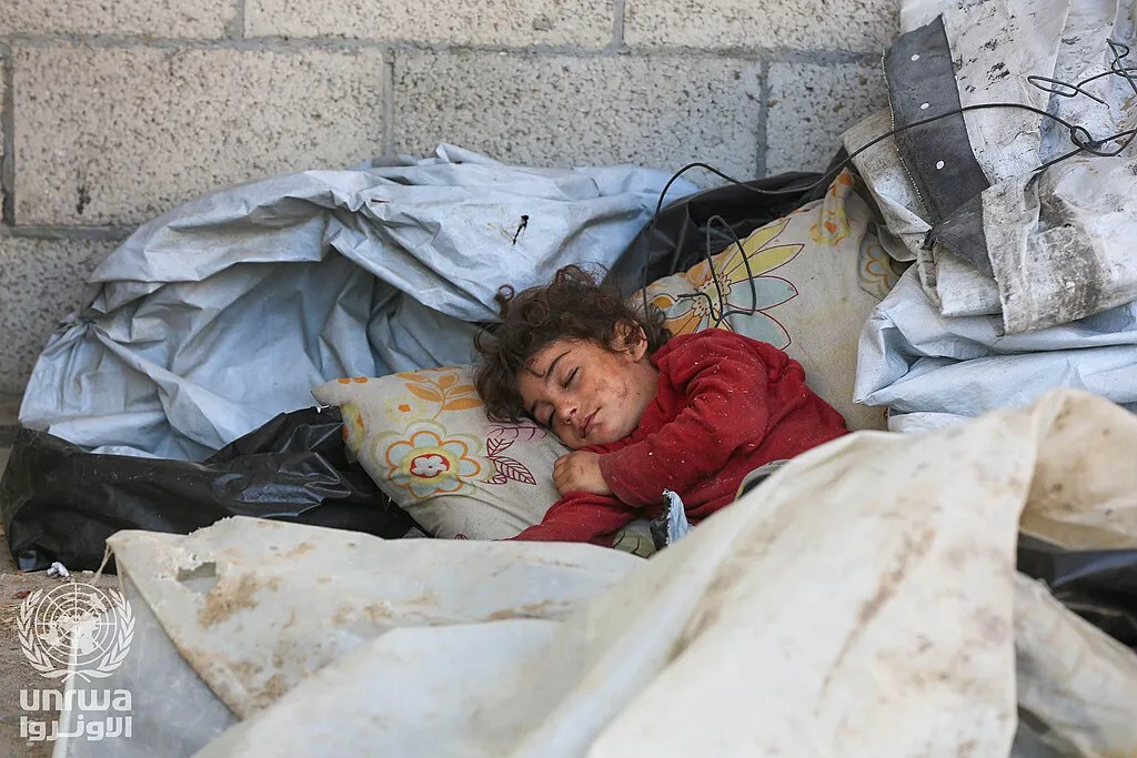 A displaced Palestinian girl sleeps outdoors among makeshift bedding in Deir el-Balah, Gaza Strip