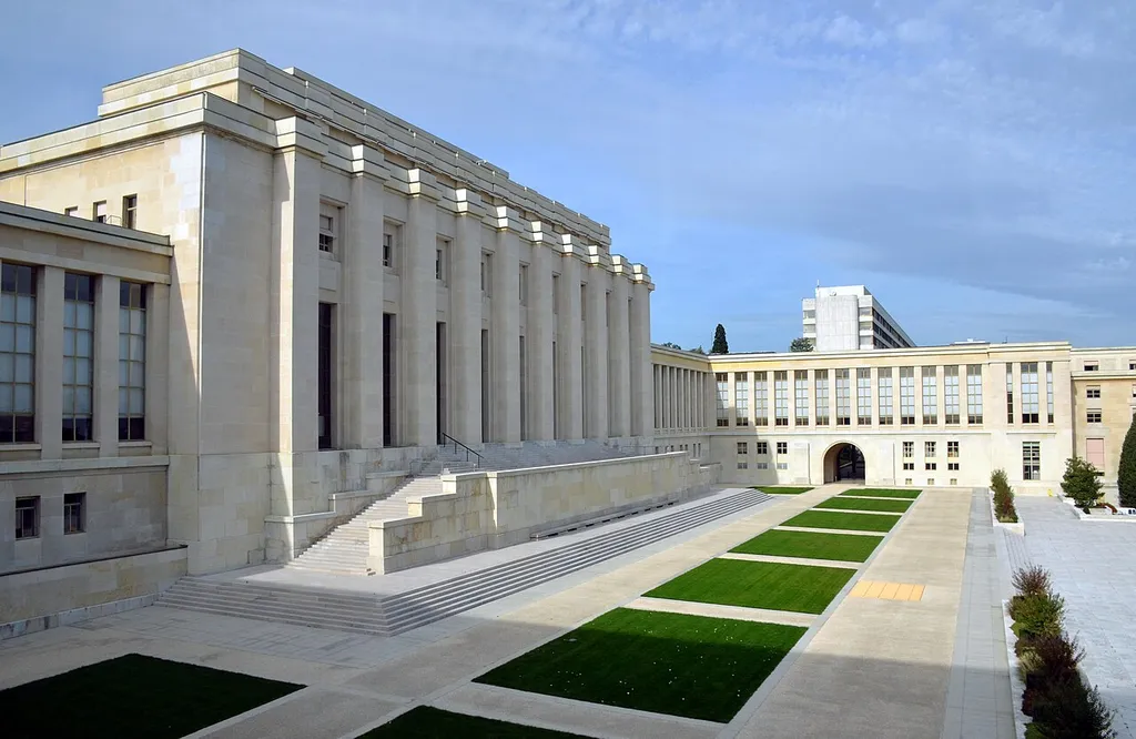 Exterior of the Palais des Nations in Geneva, home of the UN Office at Geneva, with its stone Assembly Hall facade and courtyard lawns