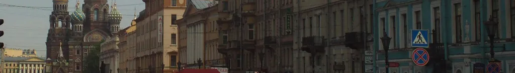 Street view in St Petersburg, Russia, with the onion domes of the Church of the Savior on Spilled Blood visible on the left among historic city buildings.