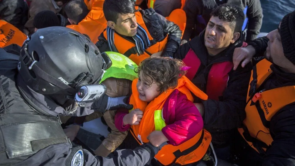 A Greek coast guard officer pulls a crying child in an orange life jacket from a crowded migrant boat at sea