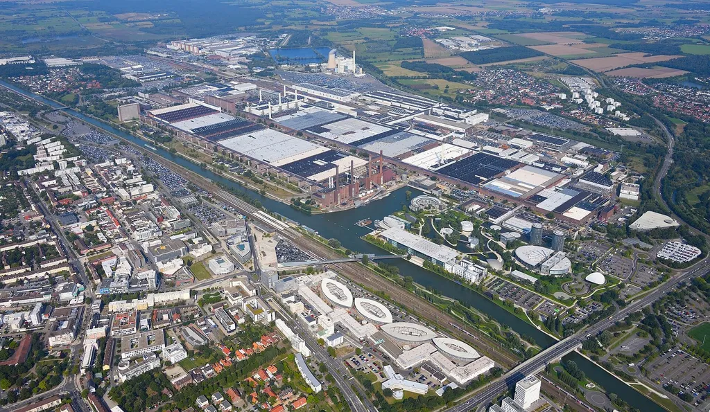 Aerial view of the Volkswagen plant in Wolfsburg, Germany, with its factory halls, power-plant chimneys and the Mittelland Canal in the foreground.