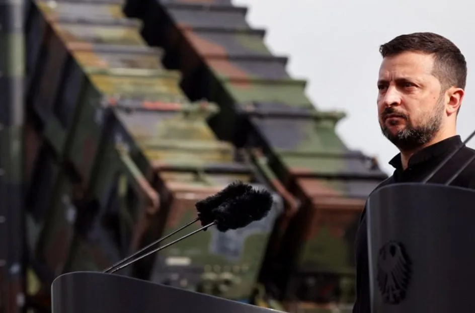 Volodymyr Zelenskyy speaking at a podium in front of a Patriot missile launcher