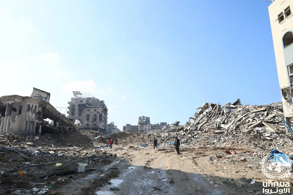 Rubble and collapsed buildings across a destroyed street in Gaza with residents walking through the debris