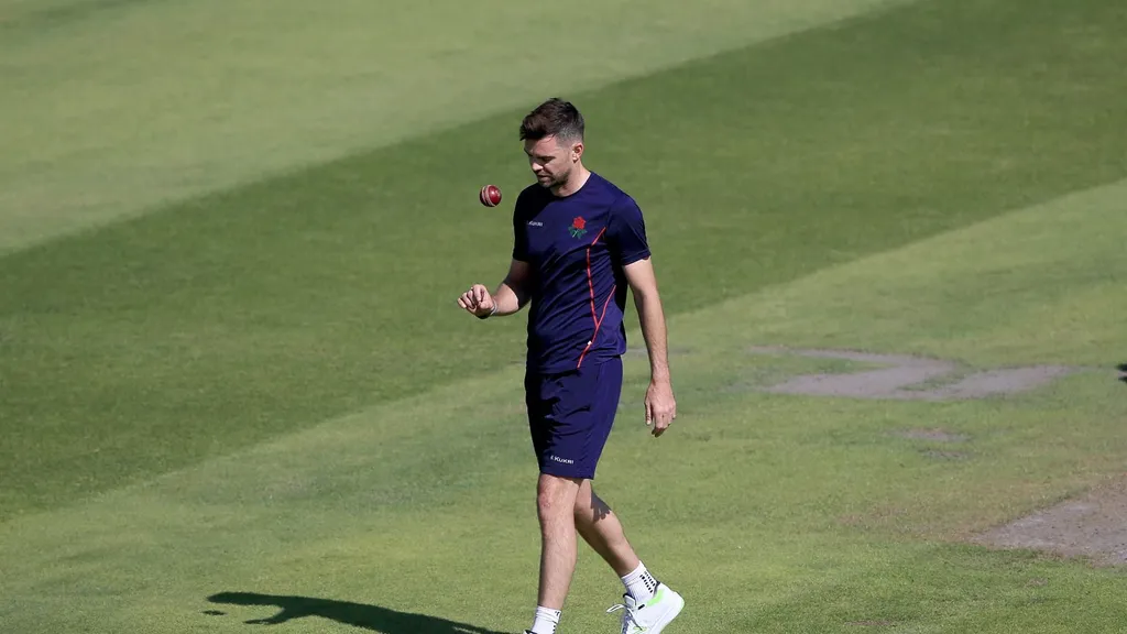 Jimmy Anderson in Lancashire training kit tossing a cricket ball on the outfield