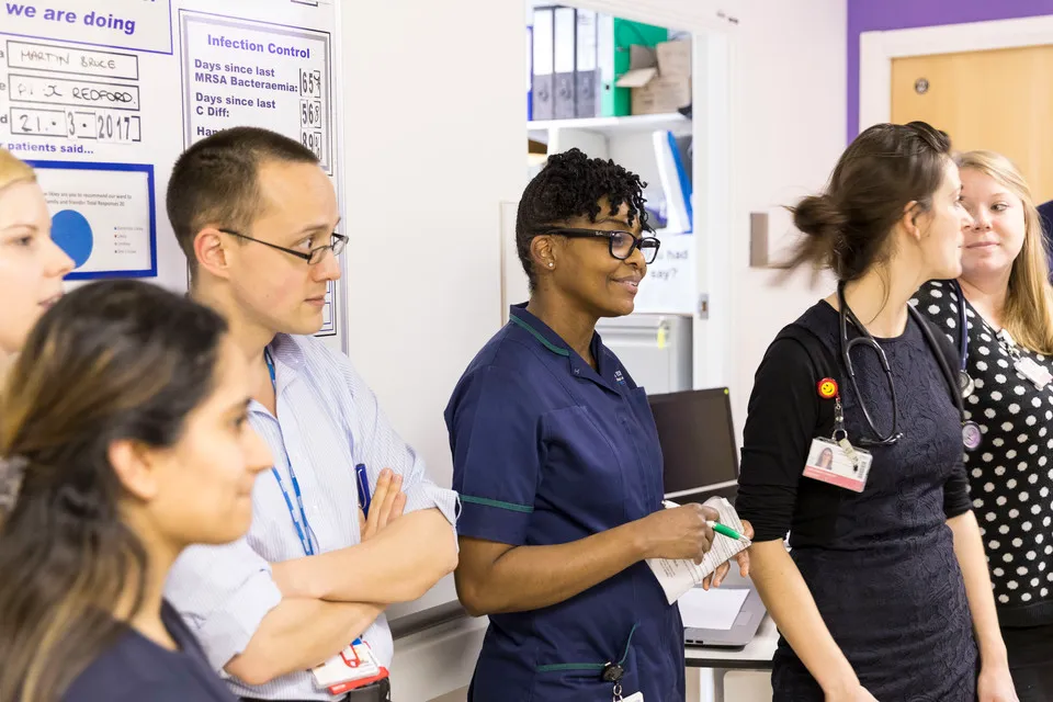 NHS doctors and nurses gathered in a hospital corridor during a team meeting