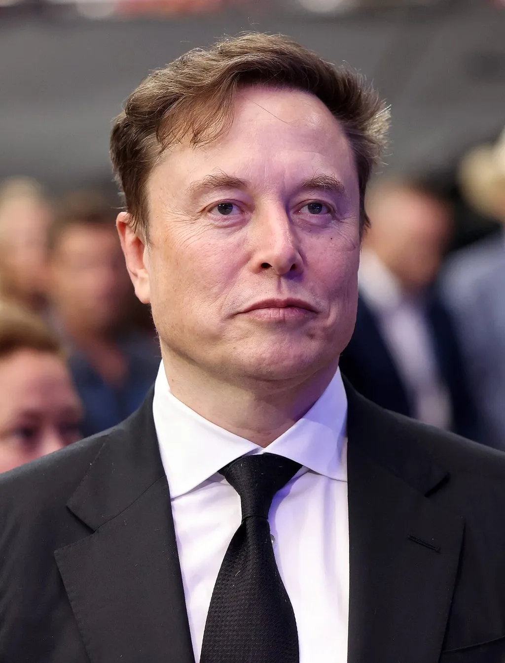 Close-up portrait of Elon Musk in a suit and tie at a public event