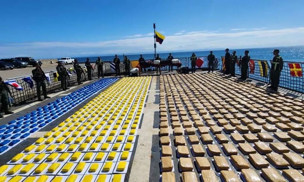 Colombian security forces standing beside thousands of seized drug packages laid out on a ship deck.