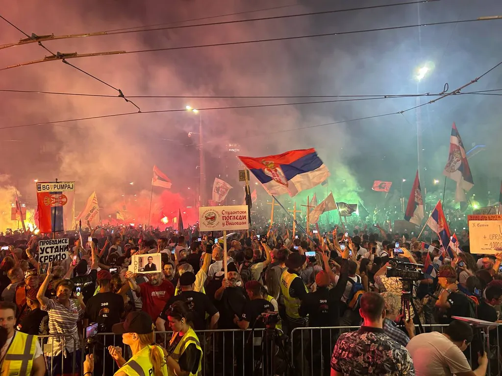 Nighttime crowd of students and citizens waving Serbian flags at a protest on Slavija Square in Belgrade