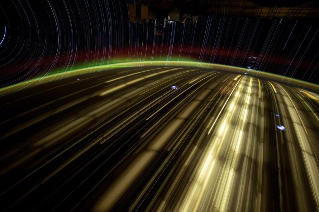 Long-exposure photograph from the International Space Station showing Starlink satellites flashing above Earth at night.