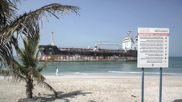 Tanker anchored off a Umm Al Quwain beach beside a bilingual beach-rules sign