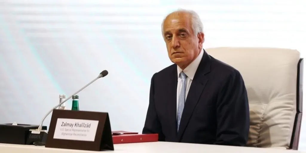 Zalmay Khalilzad seated at a conference table with his nameplate in front of him