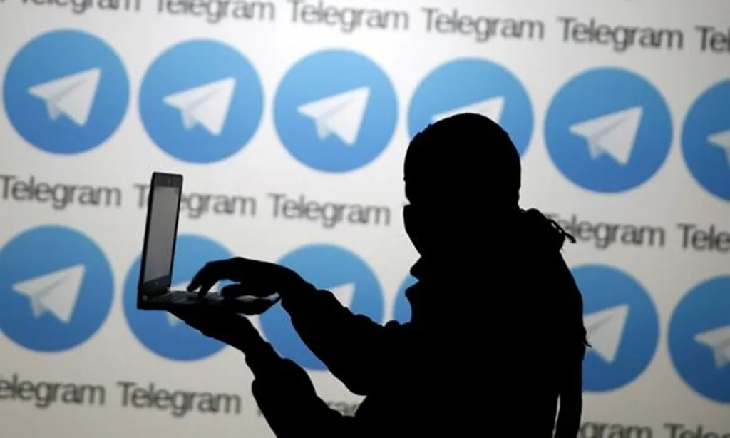 Silhouetted person using a laptop in front of a wall of Telegram logos