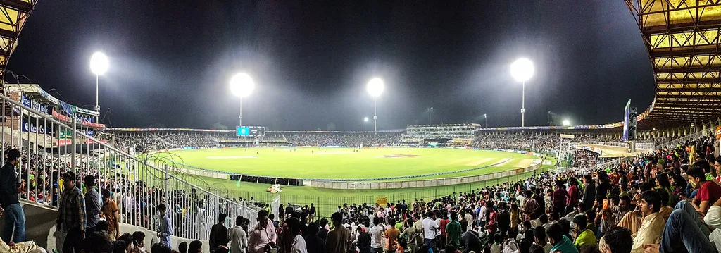 Gaddafi Stadium in Lahore at night, a floodlit cricket ground with a large crowd