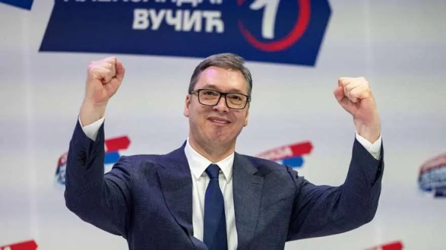 Serbian President Aleksandar Vucic raises both fists at a campaign event beneath a banner bearing his name