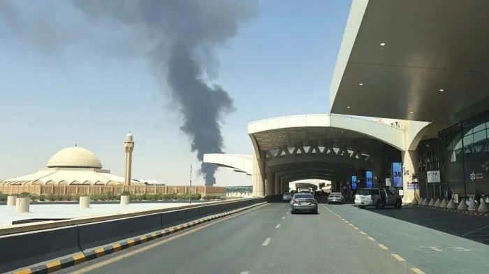 Black smoke rising near Riyadh airport terminal after a Houthi attack, with cars on the airport road