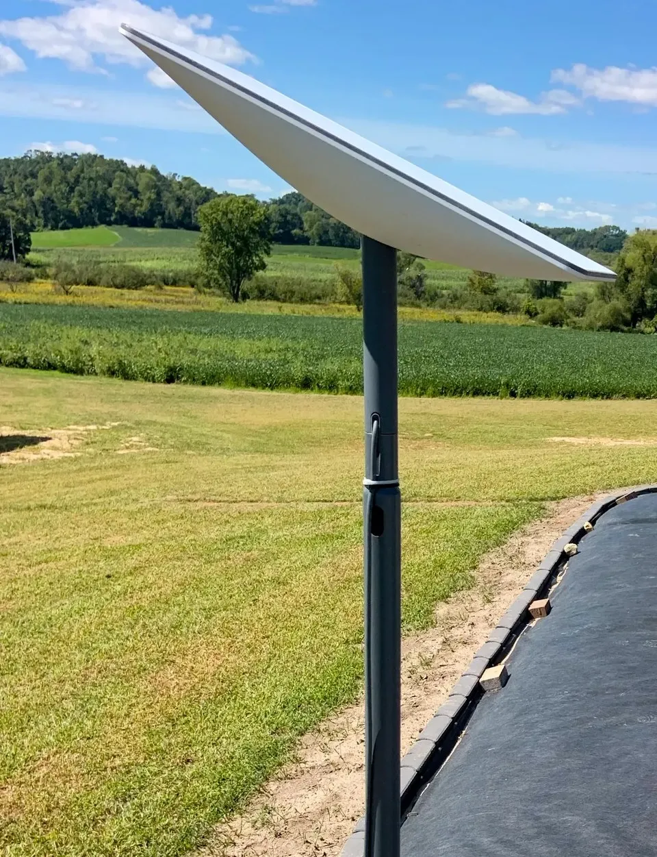 A Starlink satellite dish on a pole mount against a blue sky above rural fields.