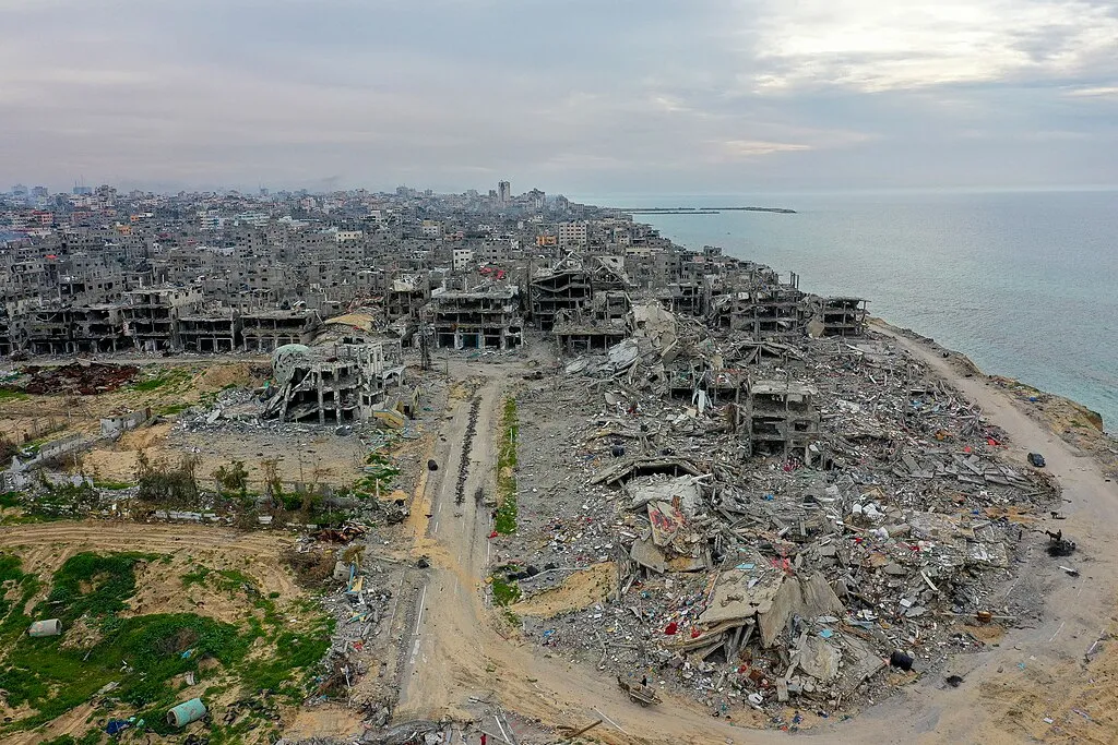 An aerial view of destroyed buildings and rubble in the Beach refugee camp area of the Gaza Strip, with the sea beyond.