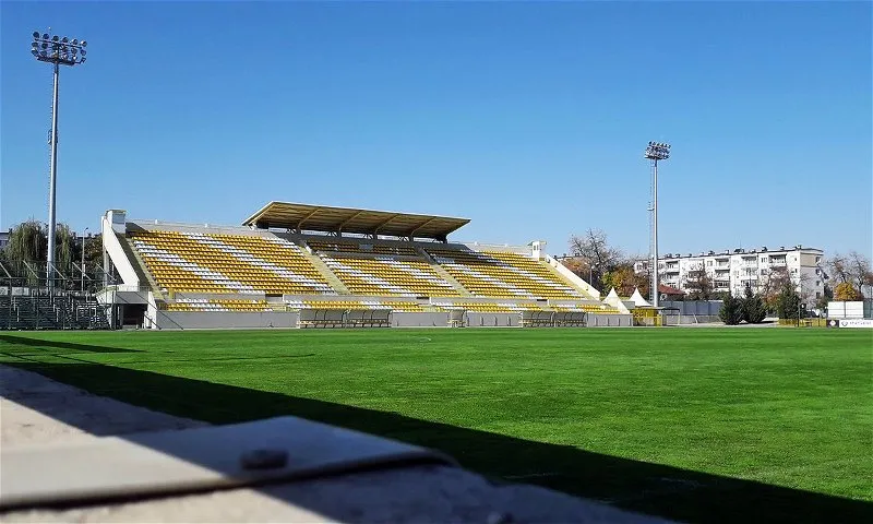 Botev Plovdiv's stadium in Plovdiv, Bulgaria, with yellow seats, green pitch and floodlights under a clear sky