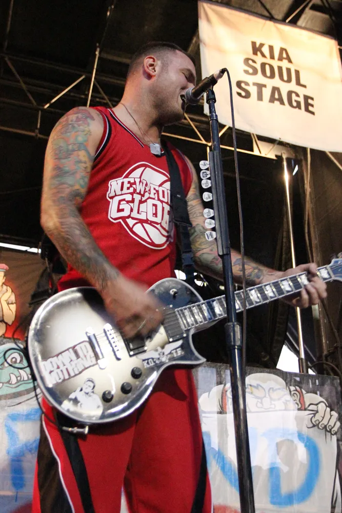 Chad Gilbert performing guitar on stage with New Found Glory at Warped Tour 2012, wearing a red New Found Glory jersey