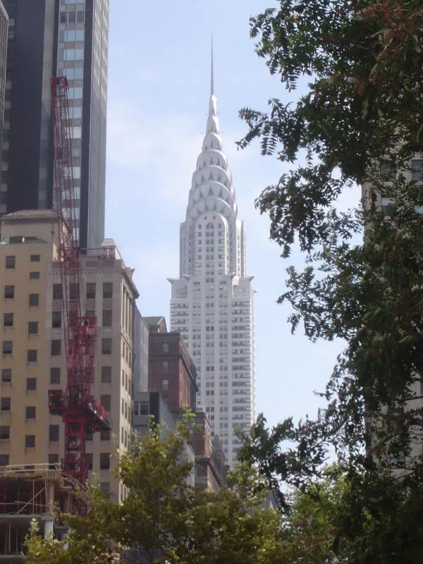 The Chrysler Building's terraced art-deco crown and spire rising above Midtown Manhattan, framed by trees and neighbouring towers.