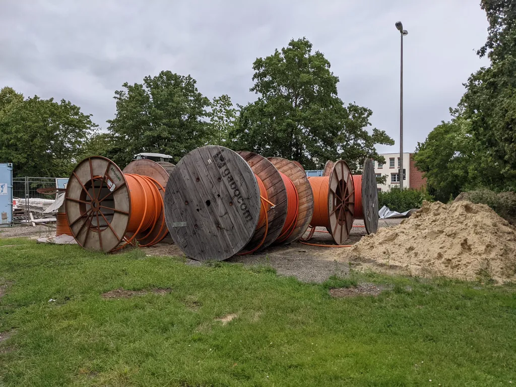 Wooden cable drums wound with orange fibre-optic conduit at a broadband construction site.