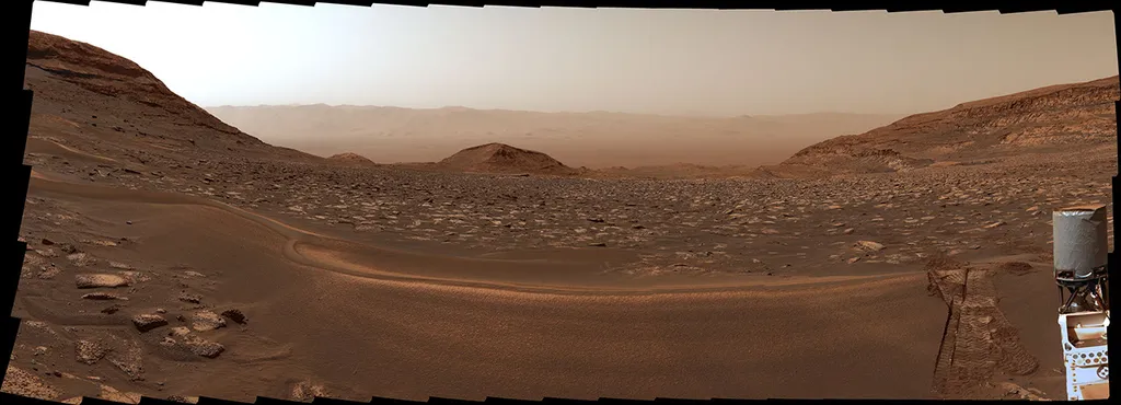 Panorama by NASA's Curiosity rover looking back across the reddish-brown floor of Gale Crater with the crater rim in the distance, a sand ridge across the foreground and the rover's right front wheel visible at right