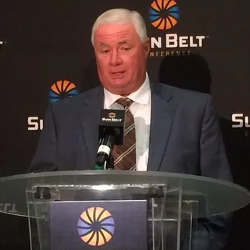 Dennis Franchione speaking at a podium during the 2015 Sun Belt Media Day