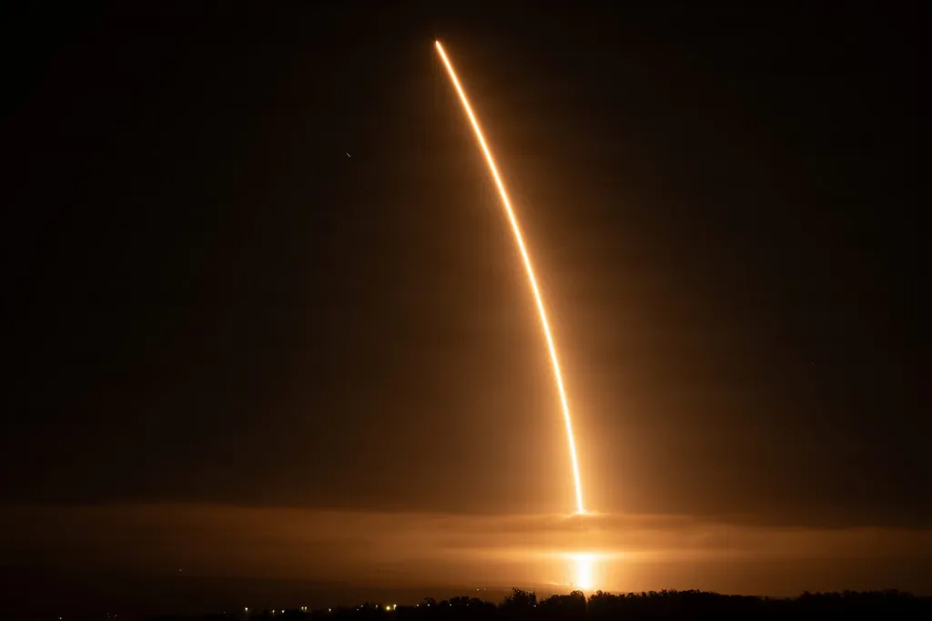 A SpaceX Falcon 9 rocket carrying Starlink satellites arcs through the night sky above Vandenberg Space Force Base