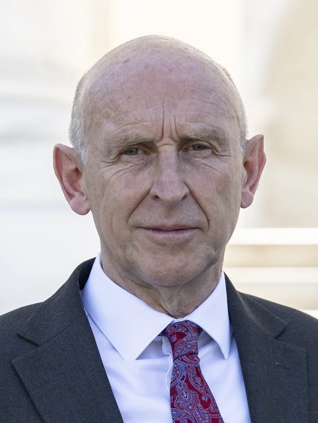 Chancellor John Healey in a dark suit and red paisley tie, photographed at Arlington National Cemetery, July 2024.