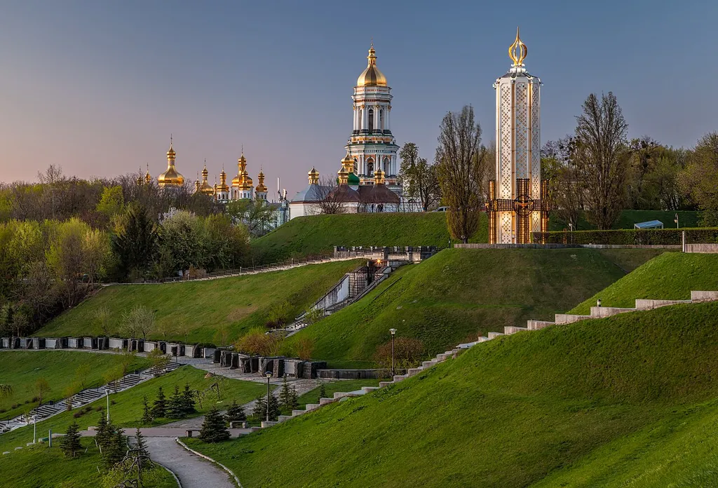 Kyiv Pechersk Lavra complex at dusk, with the Great Lavra Bell Tower and golden domes overlooking the Dnipro river in the Pechersk district.