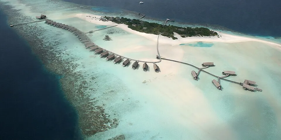 Aerial view of a Maldives island resort with overwater villas on a coral reef