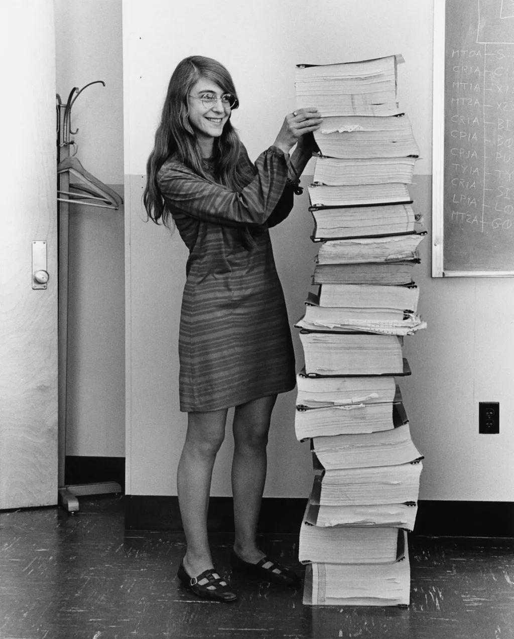 Margaret Hamilton standing beside a towering stack of Apollo Guidance Computer program listings, the software written by her and her MIT team for the Apollo Project