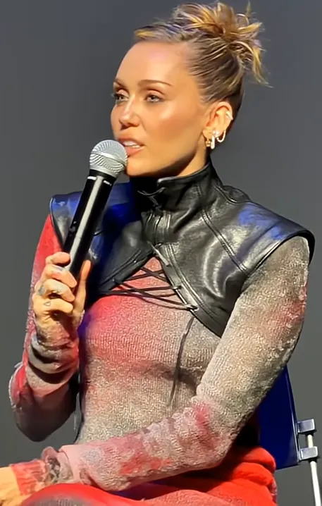 Miley Cyrus holding a microphone onstage, 2025