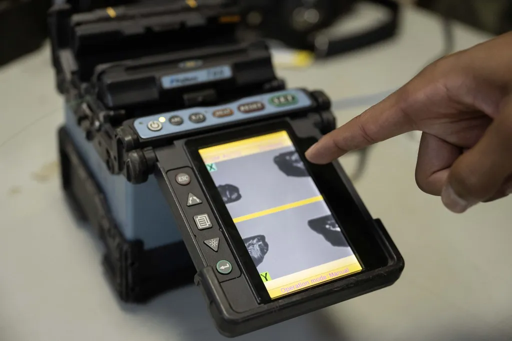 A technician's hand pointing at the screen of a fibre-optic fusion splicer