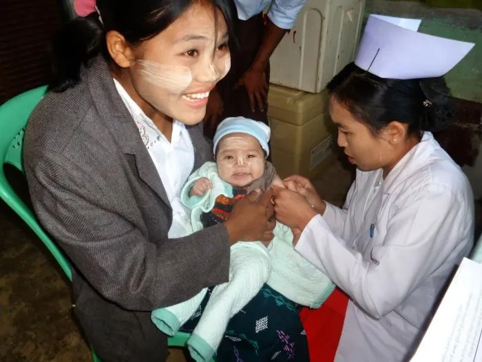 A nurse administers a measles vaccination injection to an infant held by her mother at a clinic.